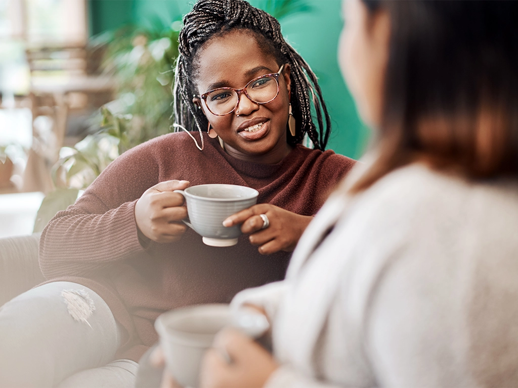 two young women having coffee and chatting on the sofa at home